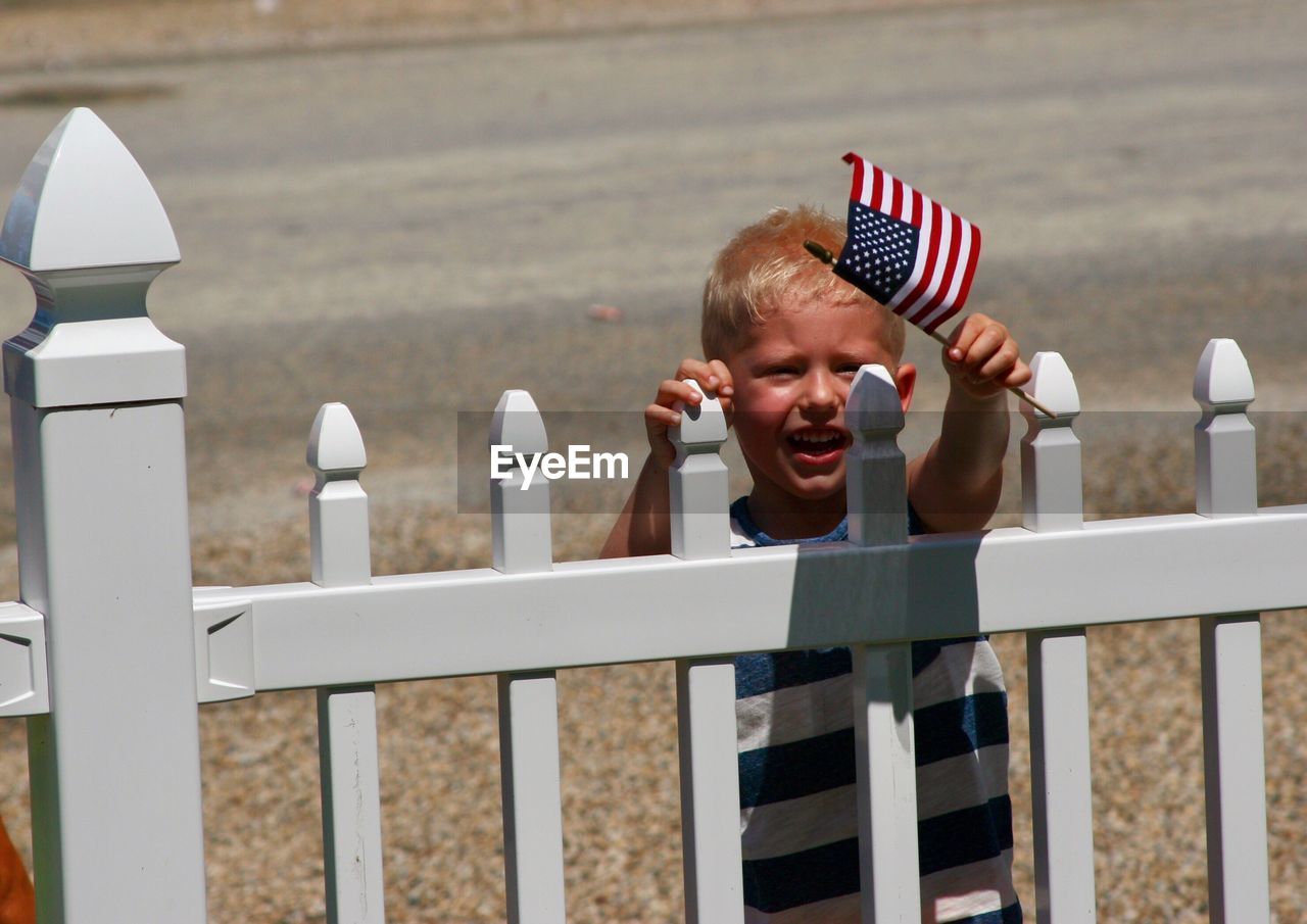 Boy holding small british flag while standing by fence