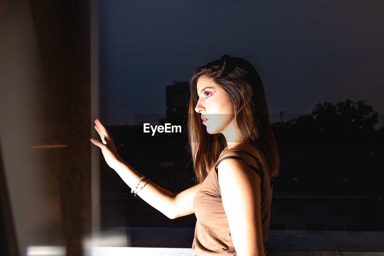 Side view of thoughtful young woman seen through window at night