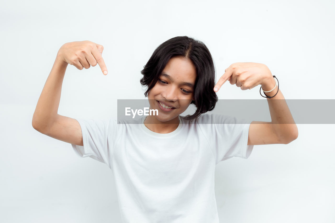 one person, finger, t-shirt, emotion, adult, studio shot, hand, white background, portrait, smiling, indoors, arm, happiness, waist up, women, flexing muscles, front view, casual clothing, positive emotion, arms raised, limb, cheerful, lifestyles, young adult, human limb, person, gesturing, cut out, vitality, female, white, muscular build, hand raised, relaxation, human face, standing, photo shoot, looking at camera, communication, fist, sleeve, clothing, excitement, strength, enjoyment, copy space, looking, fun