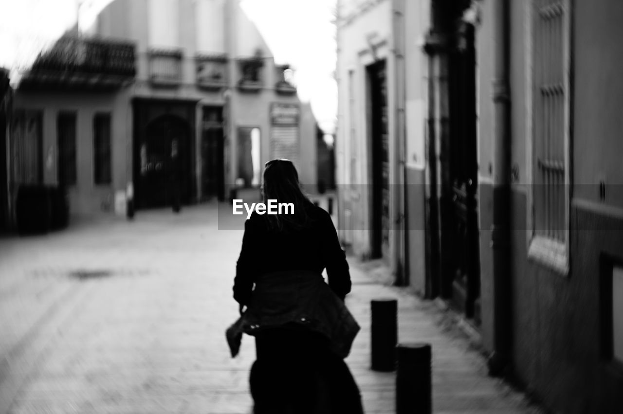 Rear view of woman walking on street amidst buildings