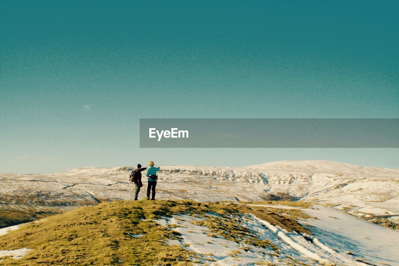 People on mountain against clear blue sky during winter