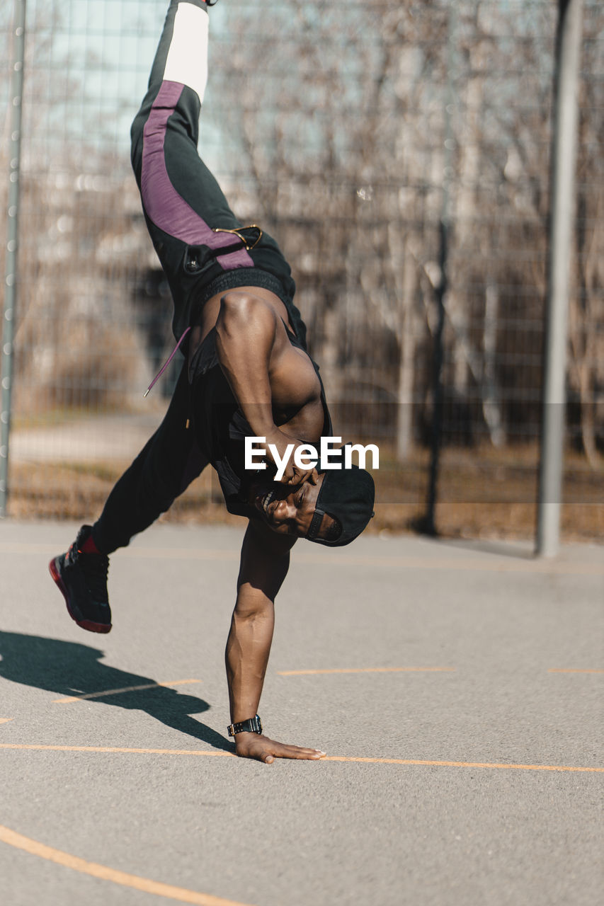 African man doing handstand while talking on mobile phone during sunny day