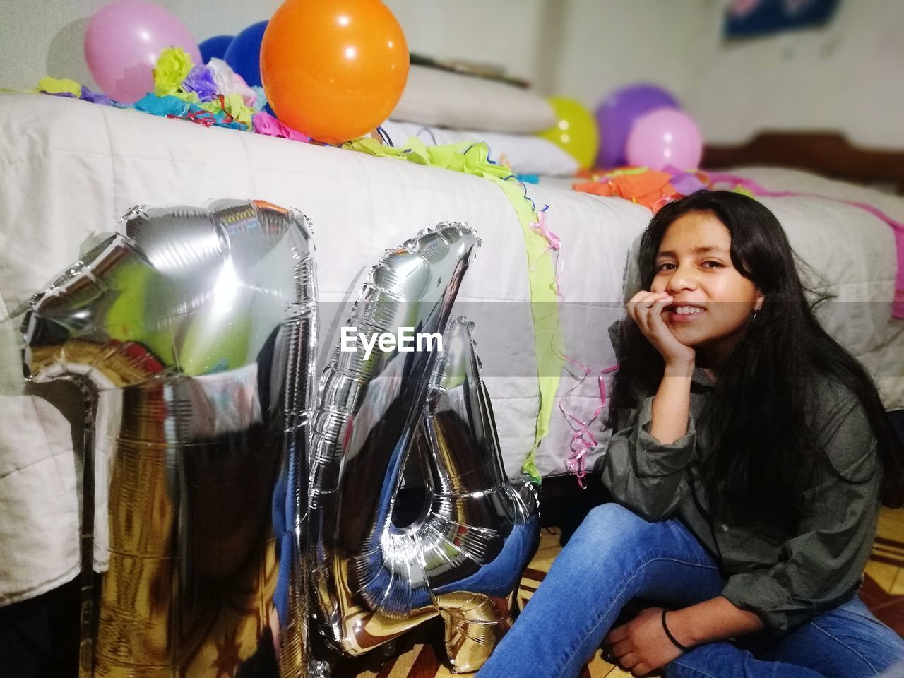 Portrait of smiling teenage girl sitting by helium balloons at home