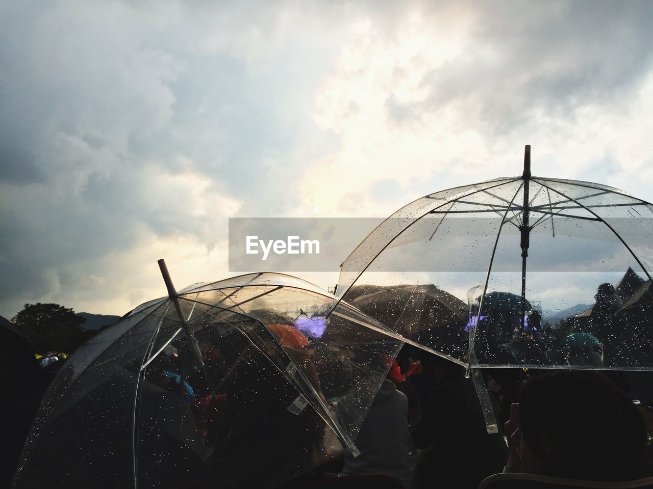 Crowd holding umbrella while standing against cloudy sky