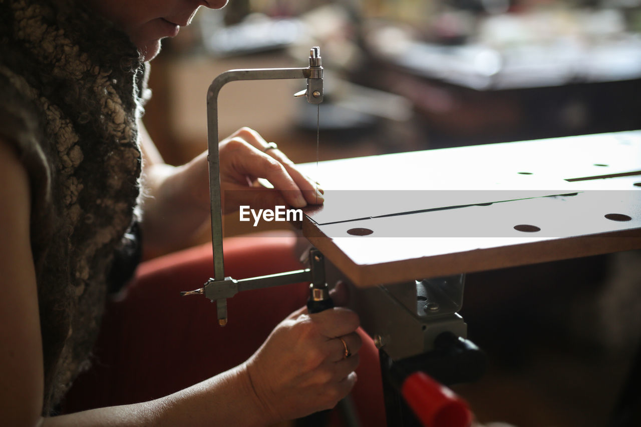 Master in the home workshop saws out a piece of copper metal with a jigsaw, concept creativity 