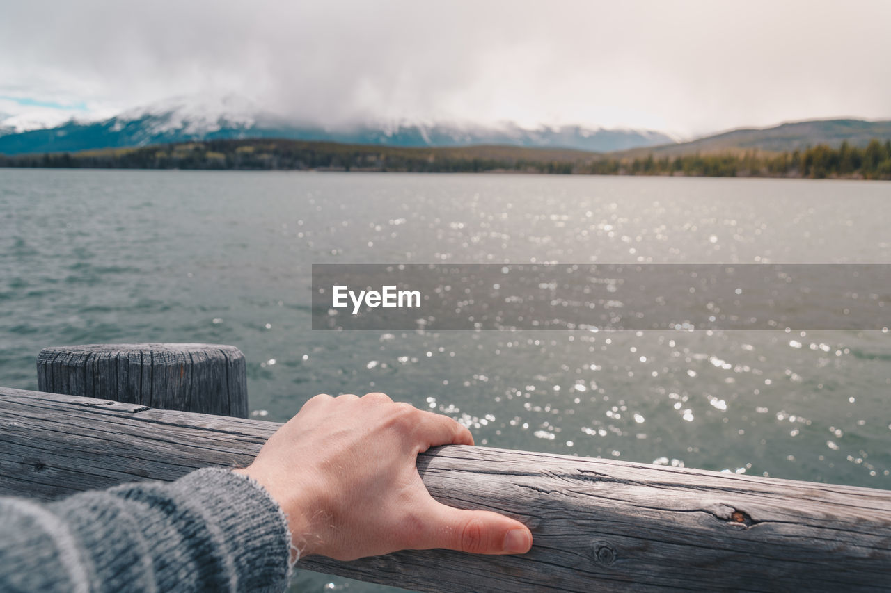 Cropped hand of person on wooden railing against pyramid lake at jasper national park