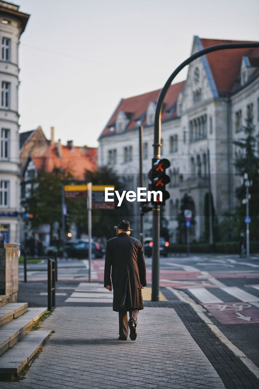 Rear view of the elegant old man walking on street against buildings in city