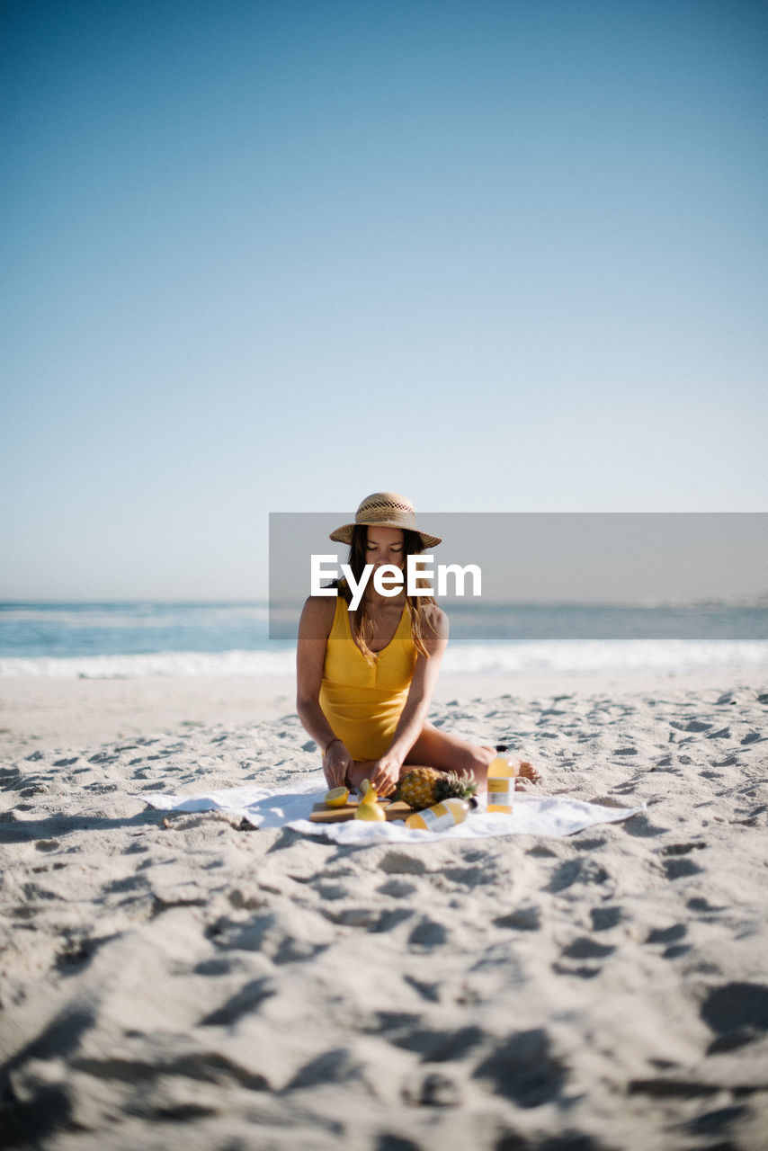 Young woman sitting at sandy beach against clear sky