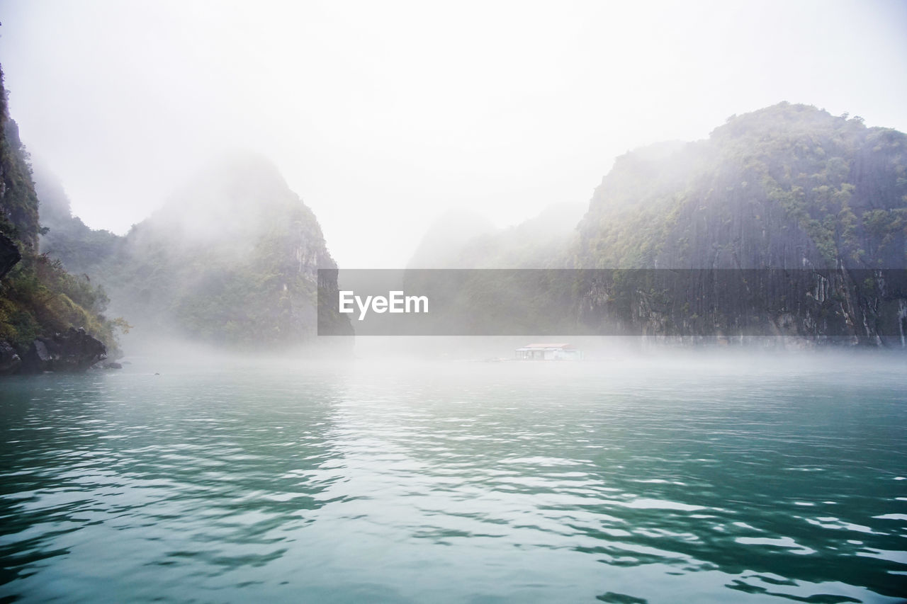 Scenic view of mountains in foggy weather at sea