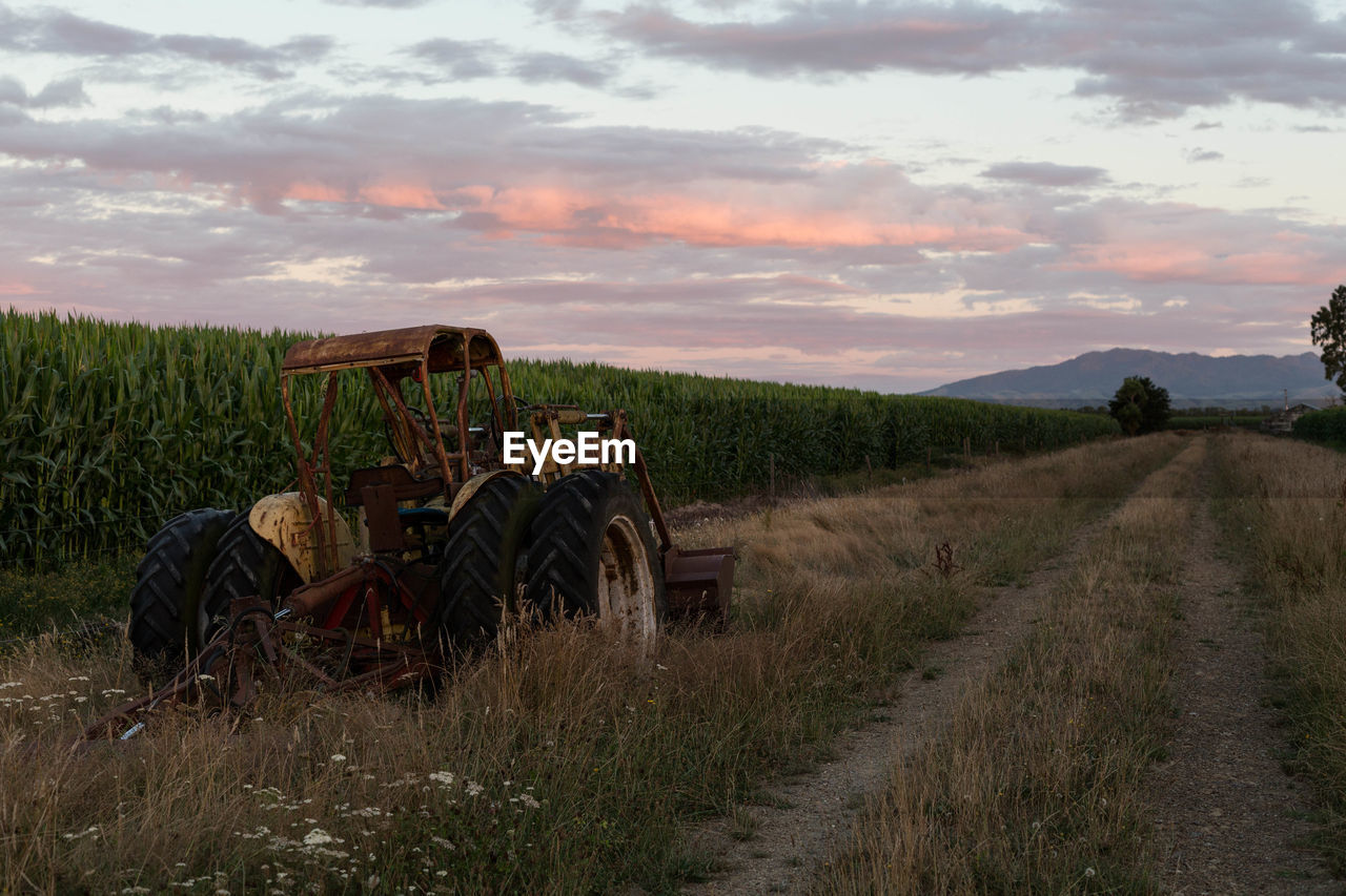 Tractor in farm against sky during sunset