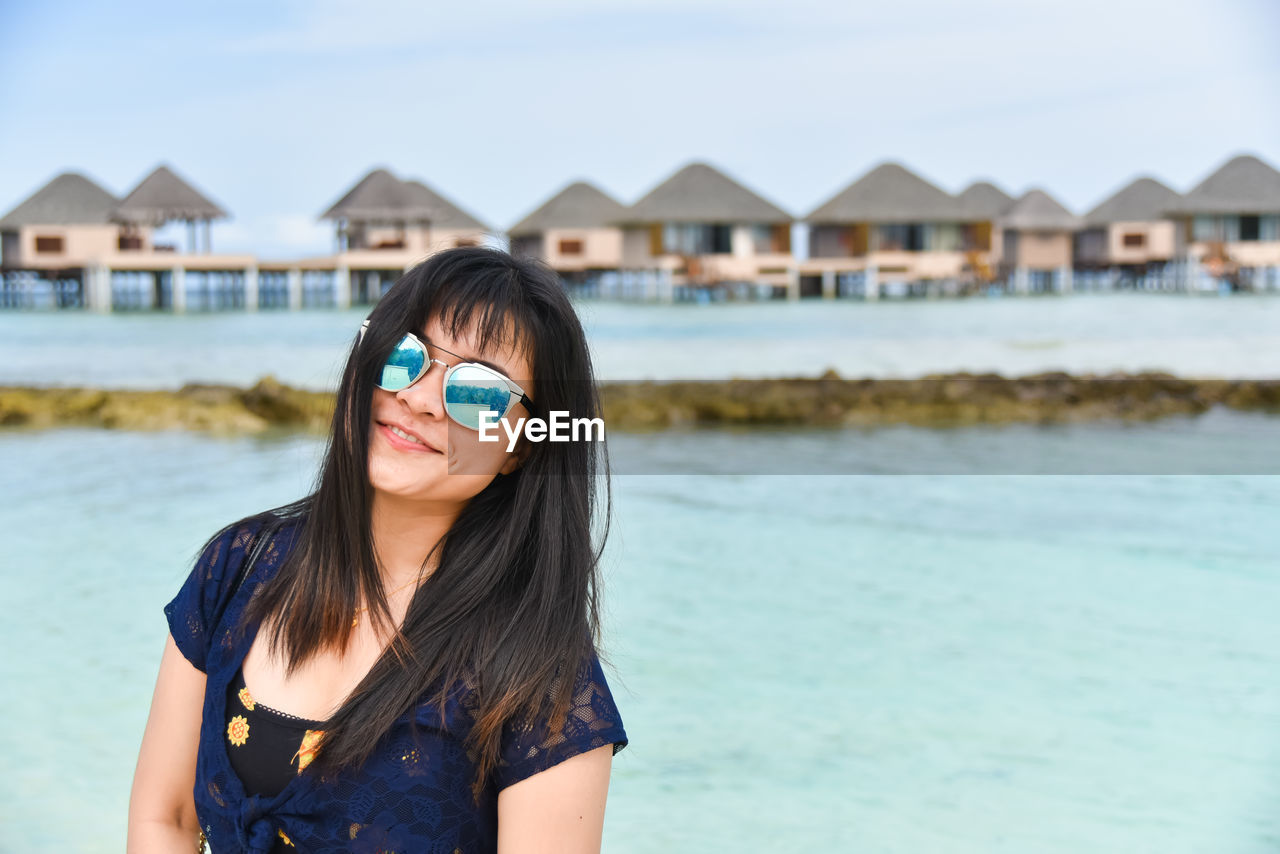 PORTRAIT OF SMILING YOUNG WOMAN AGAINST SEA