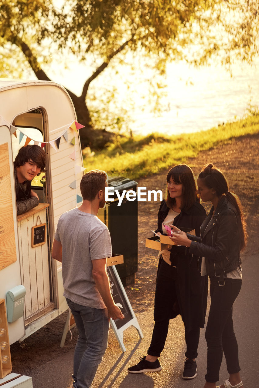 High angle view of customers and food truck owner on street during sunset