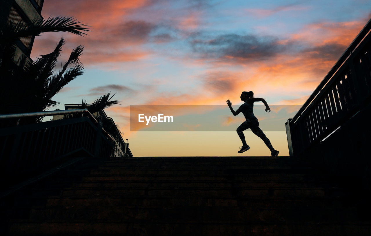 Female runner silhouette running over urban background with palm trees and sunset sky