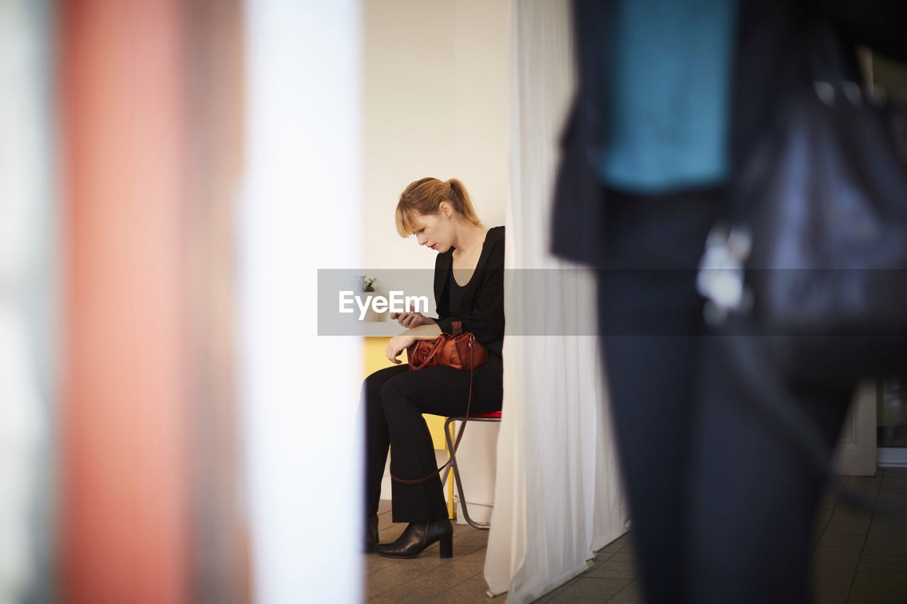 Businesswoman using mobile phone with colleague in foreground at office