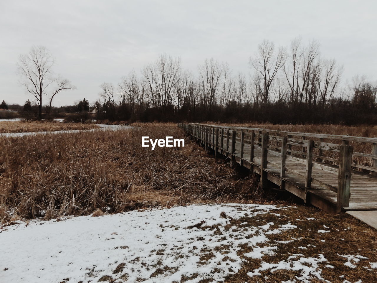 Boardwalk over field during winter against sky