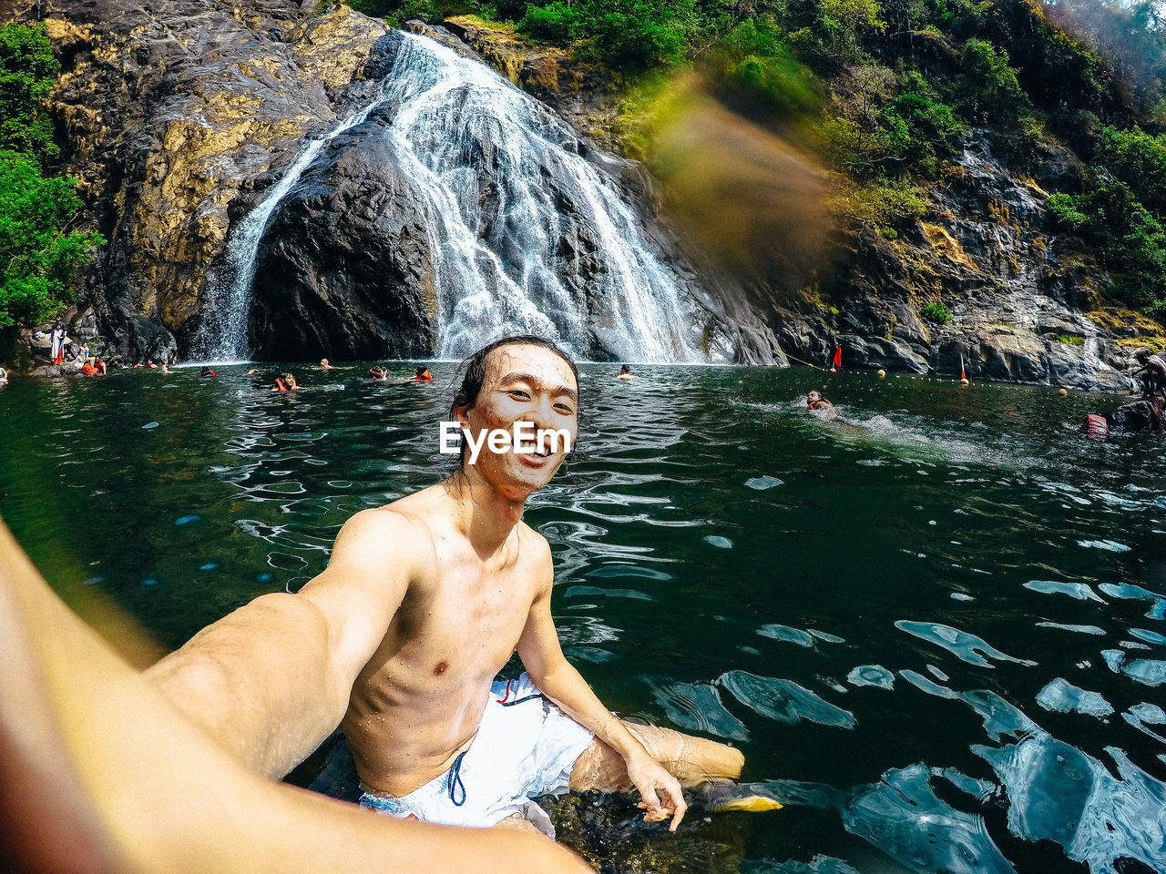 Portrait of shirtless young man looking at waterfall