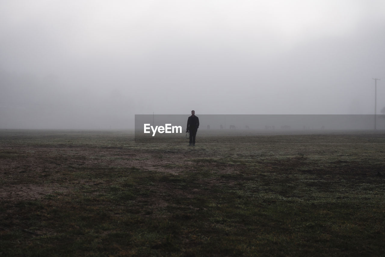 Full length of man standing on landscape against sky during foggy weather