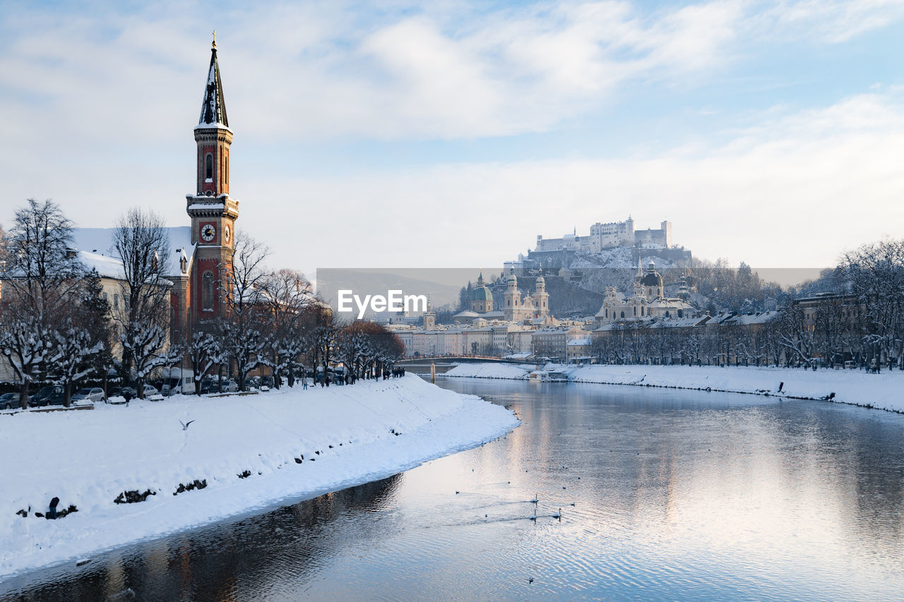 River by town against cloudy sky during winter