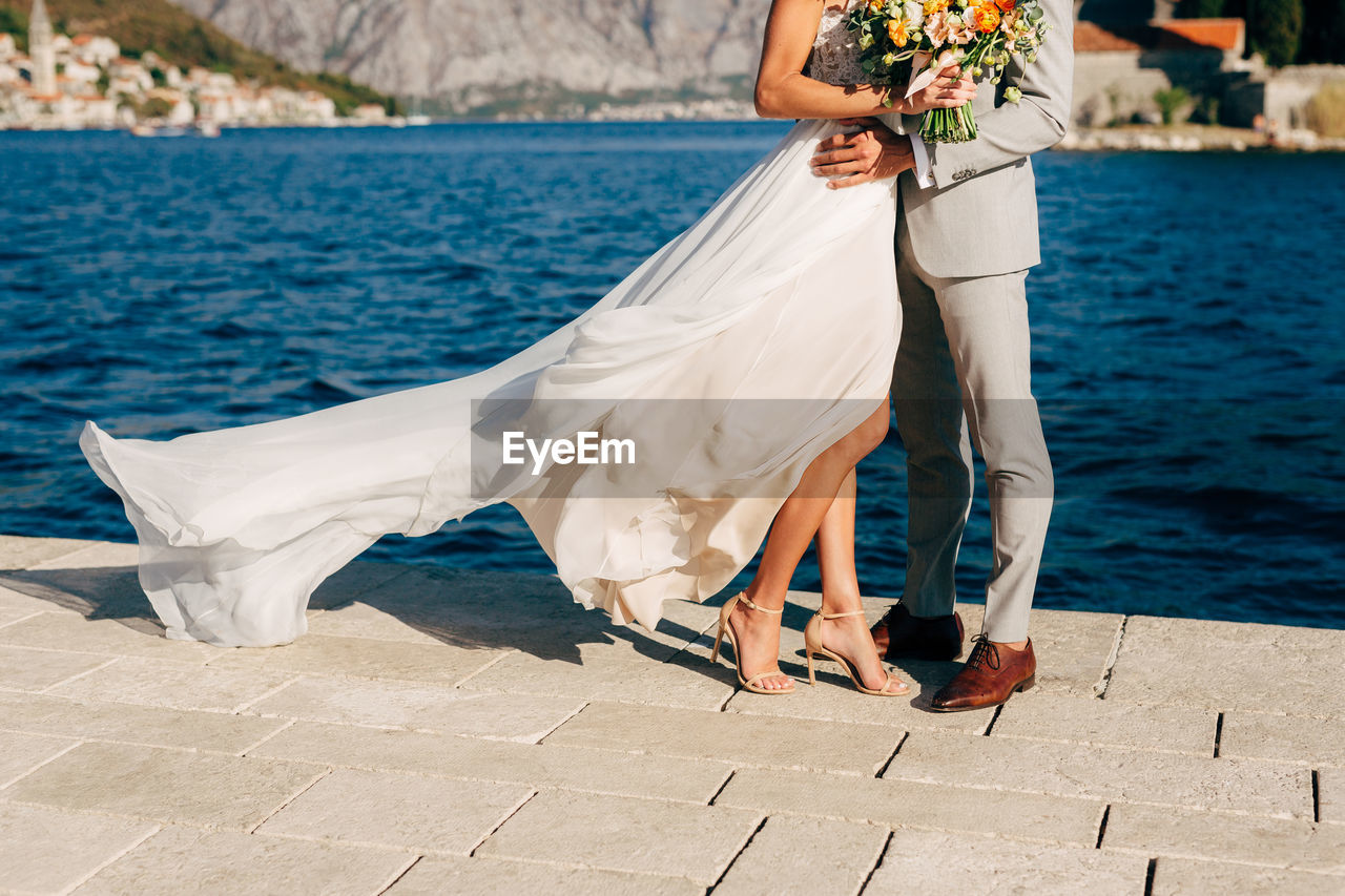 Low section of couple standing on pier by sea