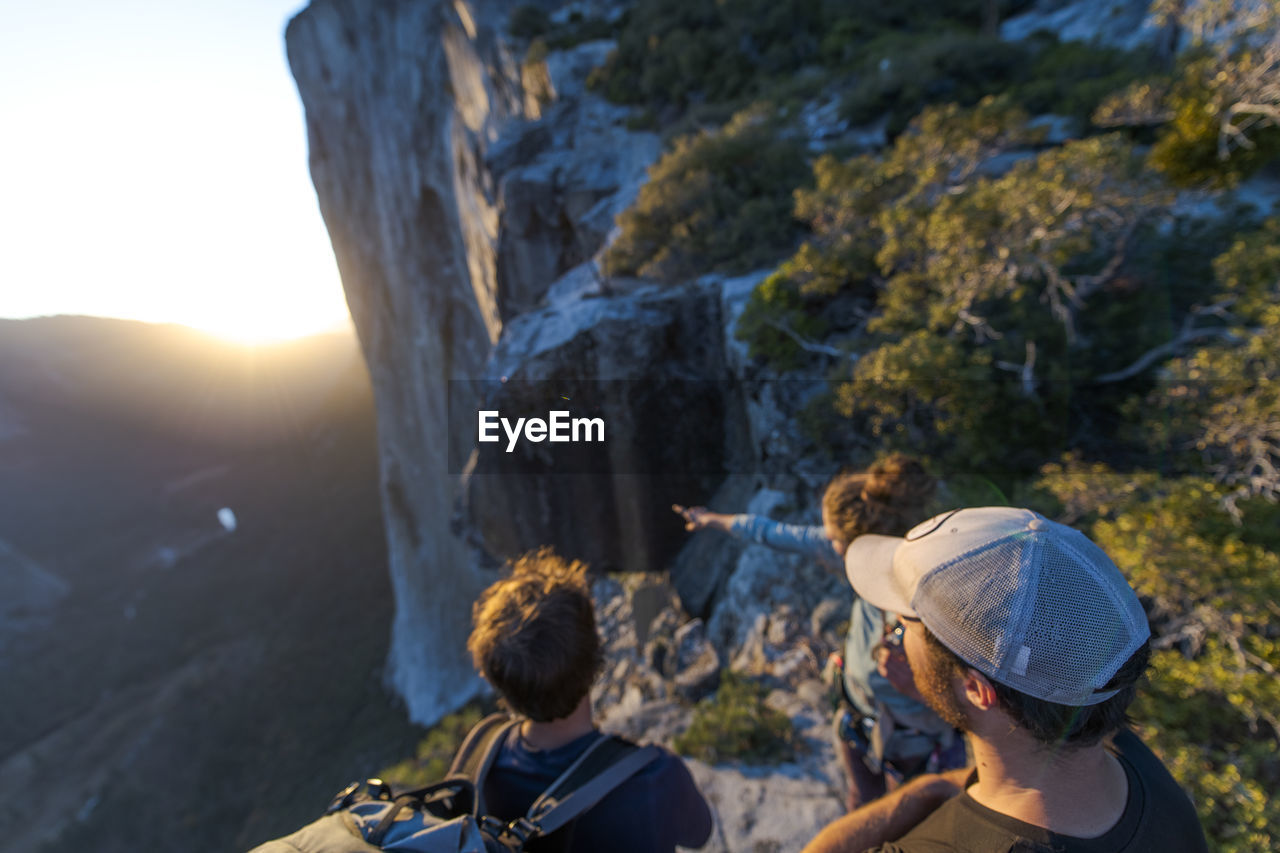 Three hikers looking at the nose el capitan from the top at sunset