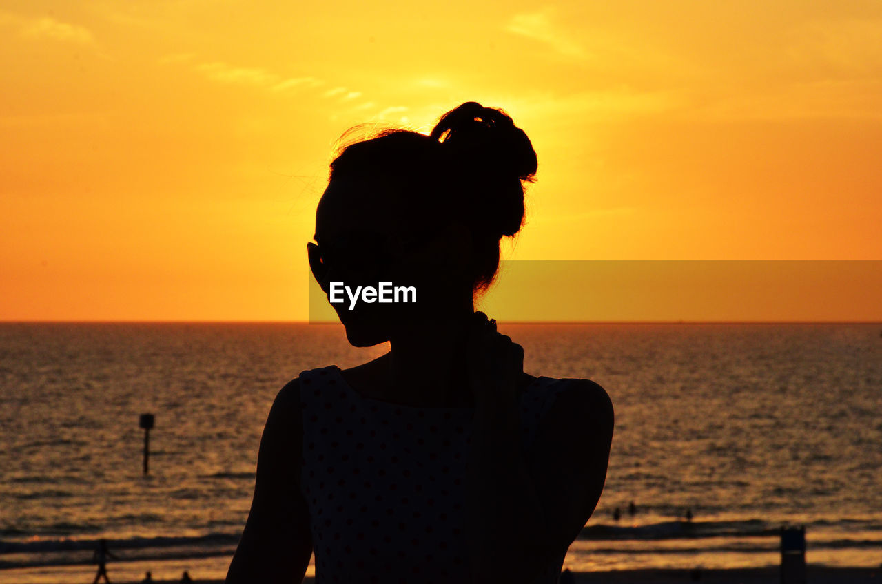 Rear view of silhouette woman standing against sea during sunset