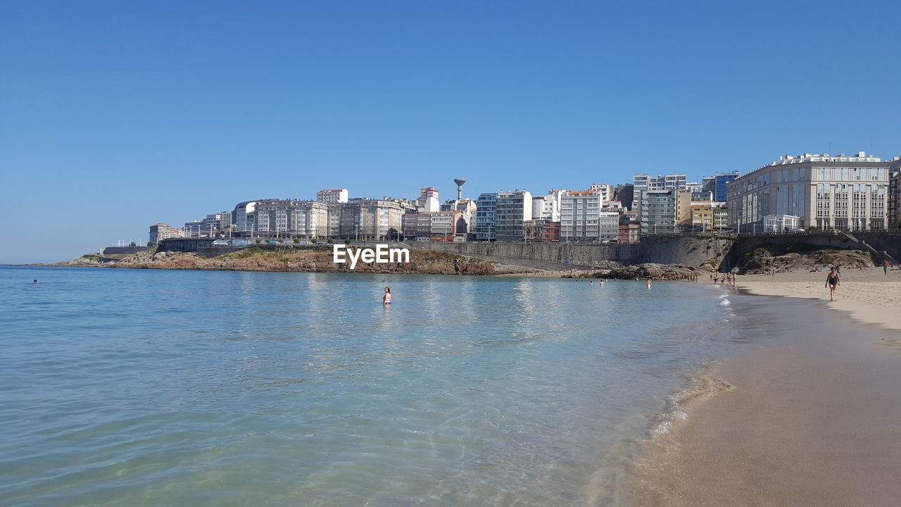 View of calm sea in front of buildings against clear sky