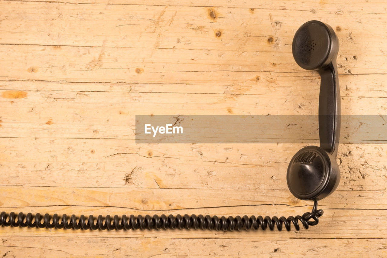 Directly above shot of black telephone receiver on wooden table