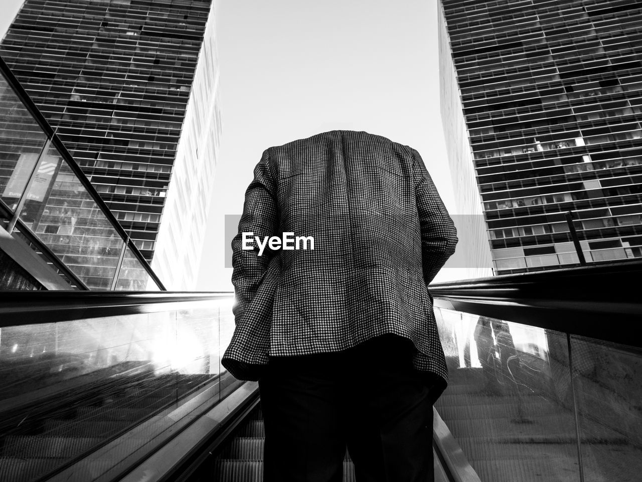 Rear view of man standing on escalator against sky