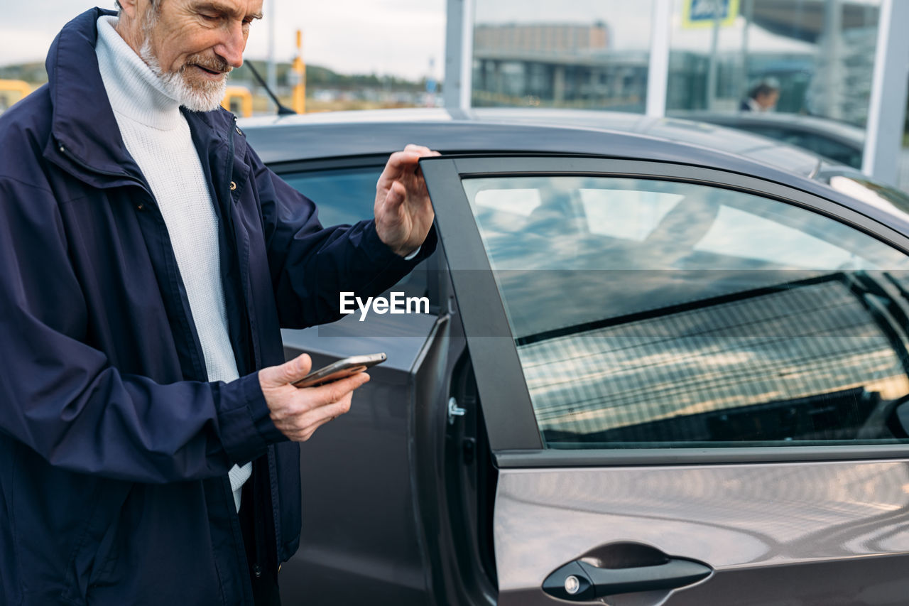 Midsection of senior man using smart phone standing by car