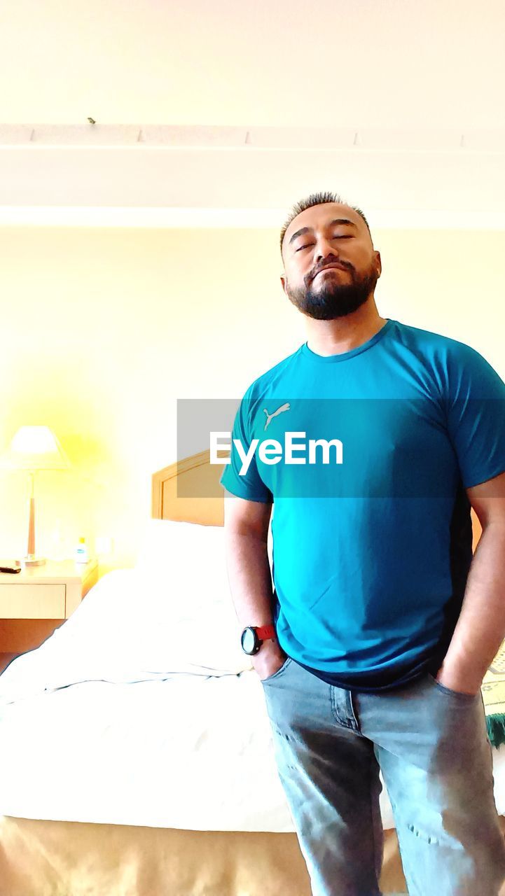 adult, men, one person, lifestyles, indoors, casual clothing, standing, three quarter length, smiling, sports, happiness, portrait, person, front view, young adult, clothing, beard, copy space, emotion, relaxation, facial hair, arm, sitting, exercising, looking at camera, blue, looking, t-shirt, vitality, cheerful