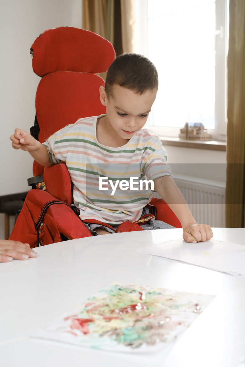 Child with cerebral palsy painting with fingers and hands. happy handicap boy developing fine motor