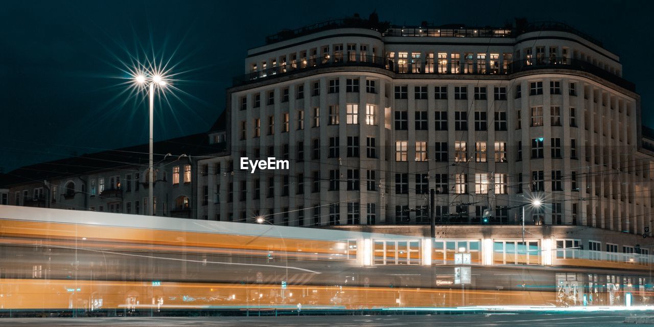 Light trails on street by buildings in city at night