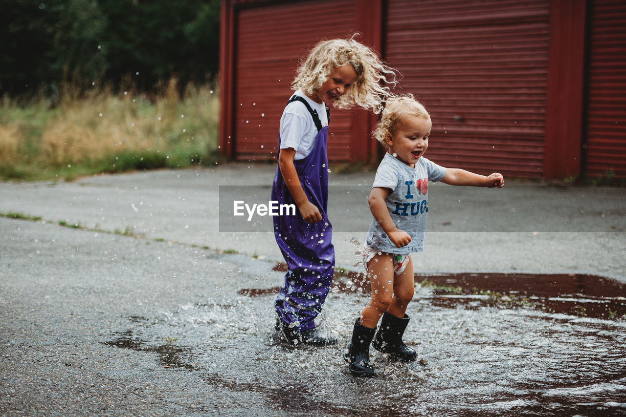 Siblings boy and girl jumping in a puddle having fun and smiling