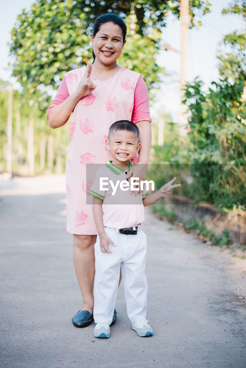 Portrait of smiling mother and son gesturing peace sign on road