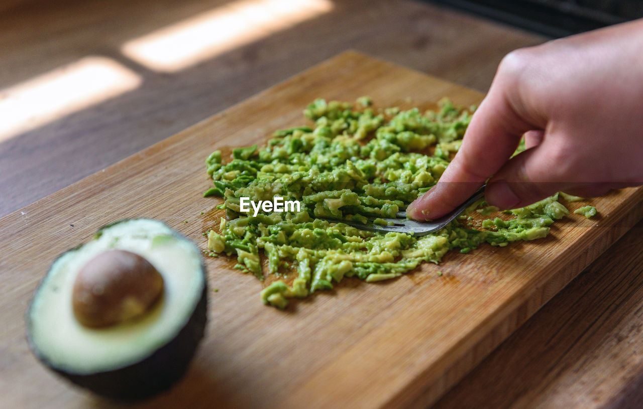 Close-up of person preparing mashed avocado on wooden cutting board