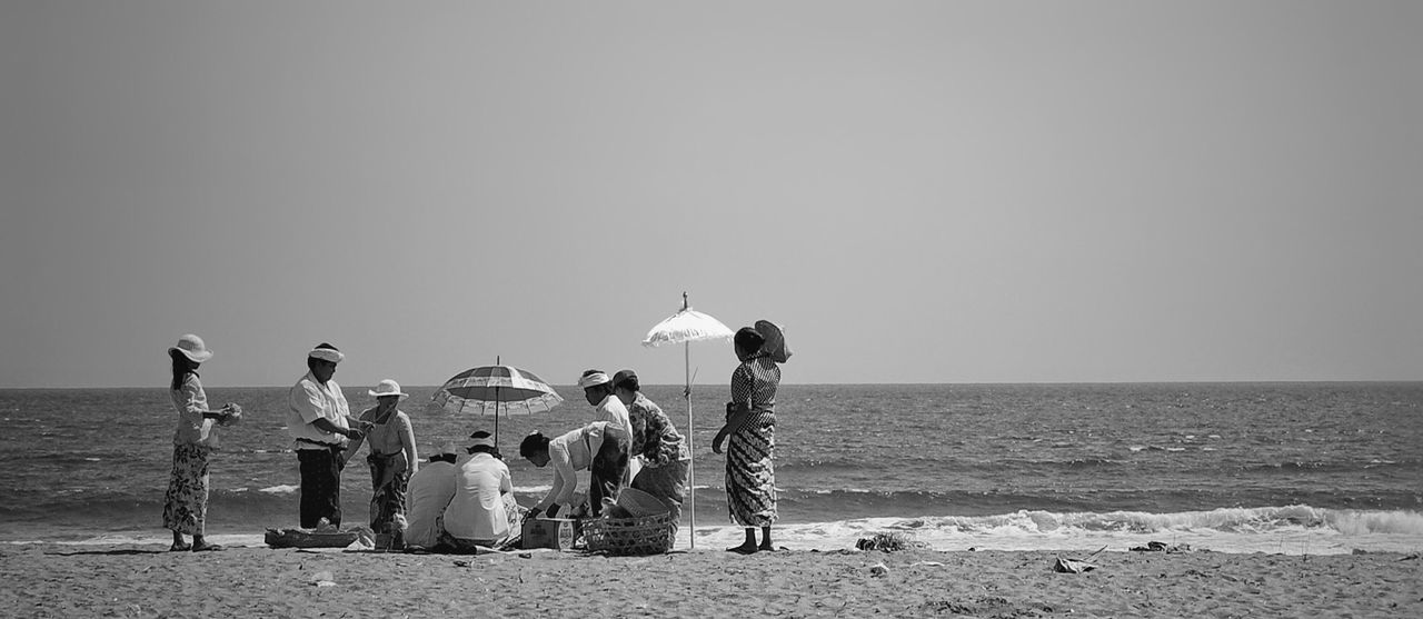 REAR VIEW OF PEOPLE STANDING ON BEACH