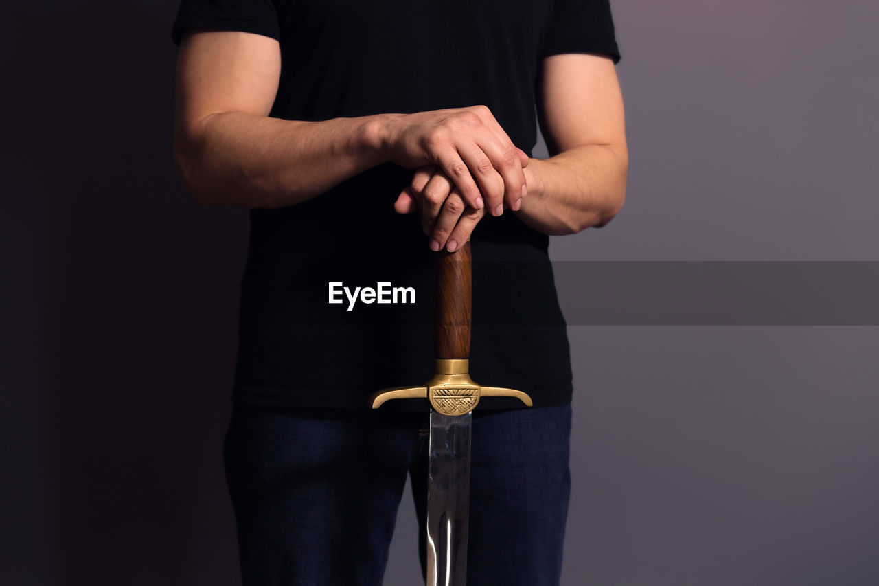 Midsection of man holding sword against gray background