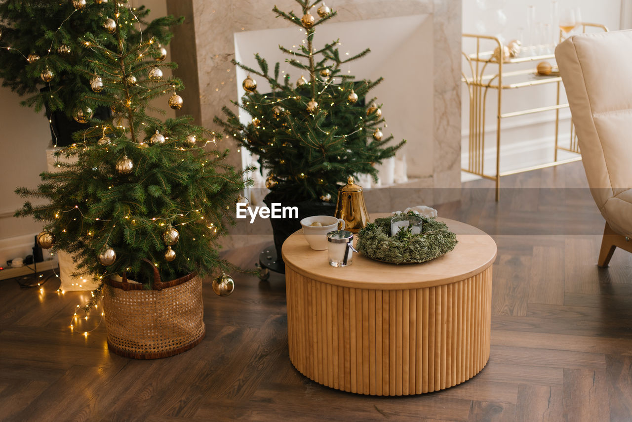 Several stylish christmas trees stand in the living room by the marble fireplace