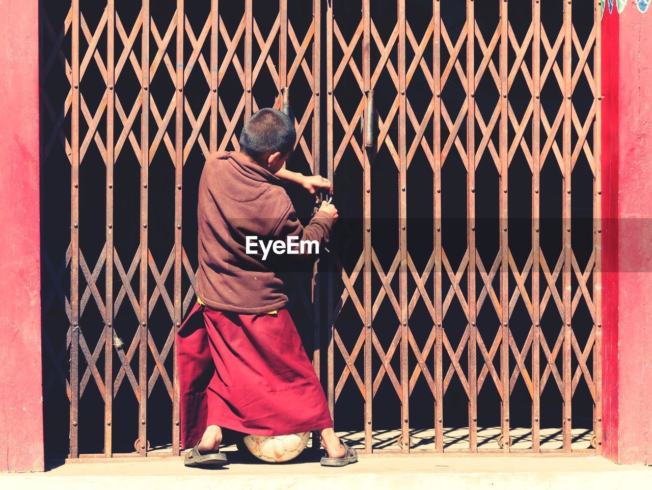 REAR VIEW OF MAN STANDING BY METAL WALL