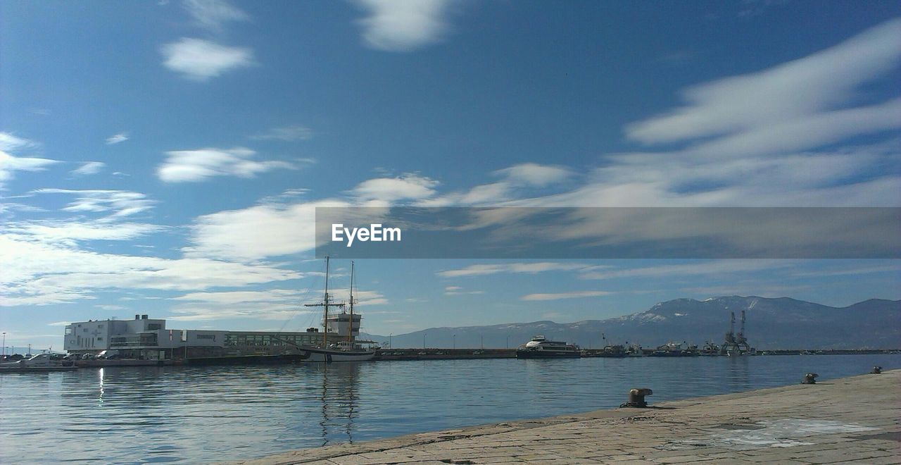 Boats at harbor against cloudy sky