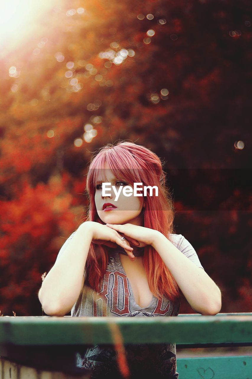 Thoughtful beautiful young woman with redhead looking away while standing by railing