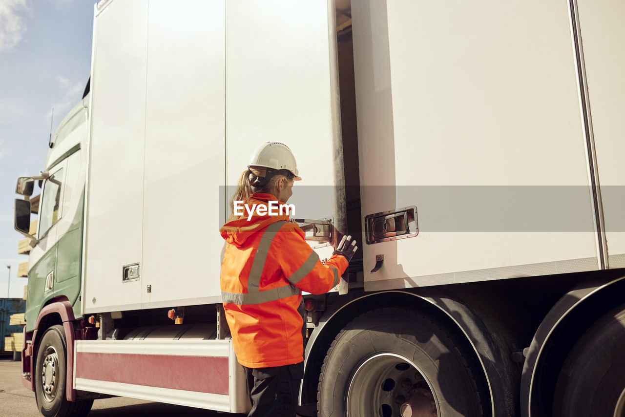 Female worker locking door of truck outside factory on sunny day