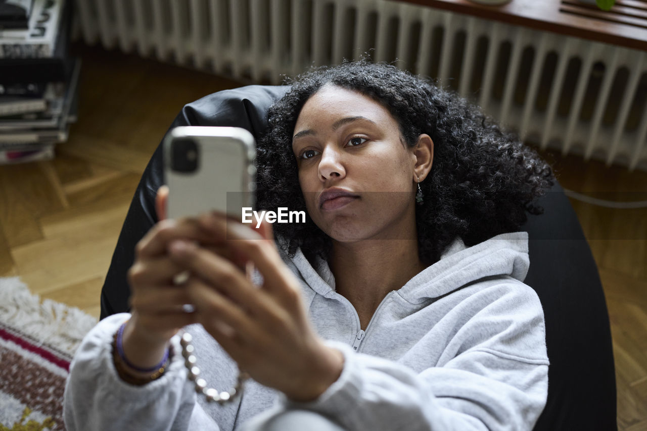 Young woman lying on bean bag and taking selfie