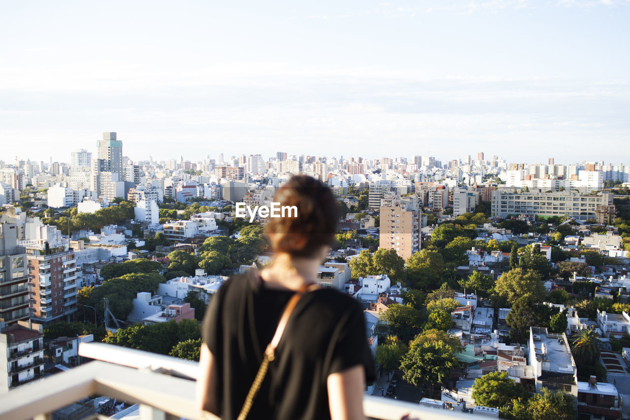 Rear view of woman standing at building terrace against cityscape