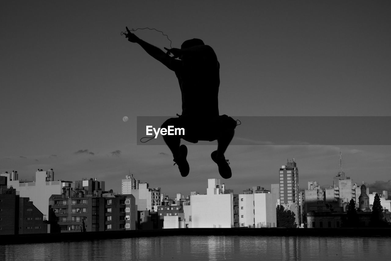 Silhouette man jumping against cityscape at dusk