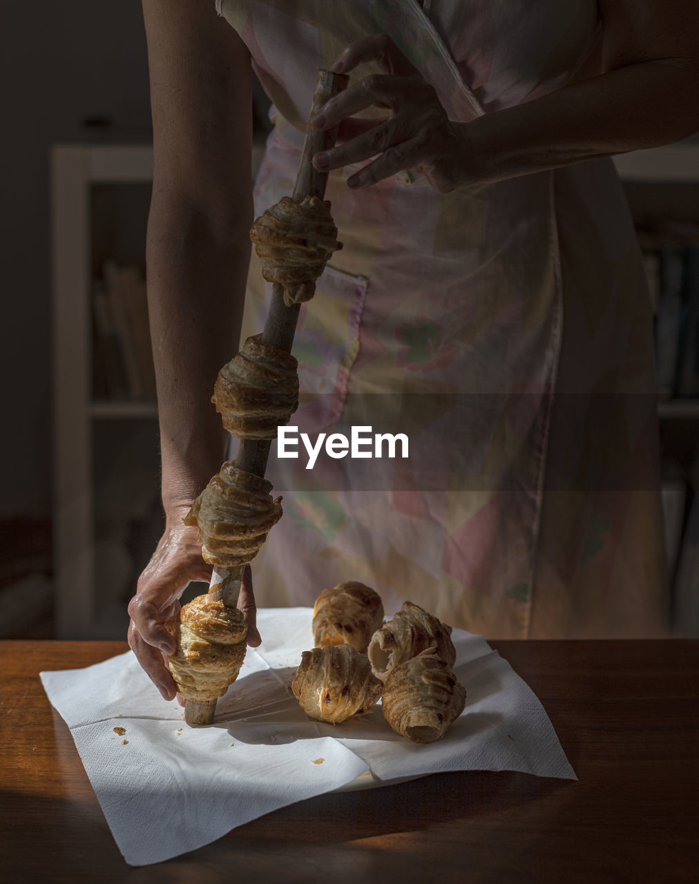 An unrecognisable woman is pulling freshly baked home-made puff pastry cannoli from a wooden stick.