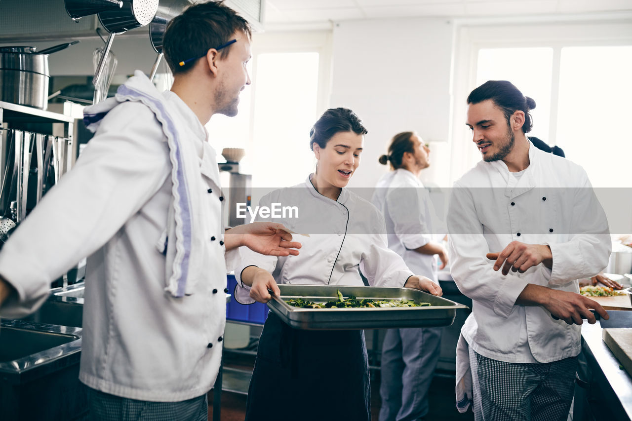 Male and female chefs discussing over food in baking sheet in commercial kitchen