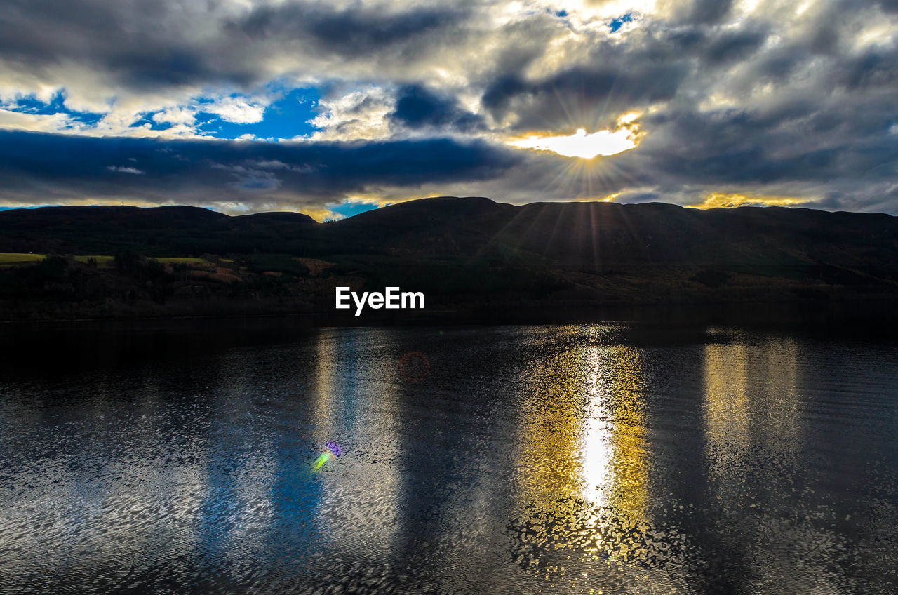 Sun shining through clouds over lake