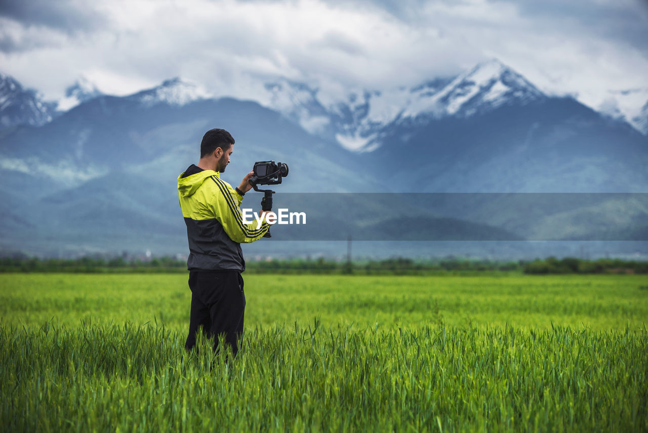 Man holding camera on a stabilizer on a green field ,scenic background