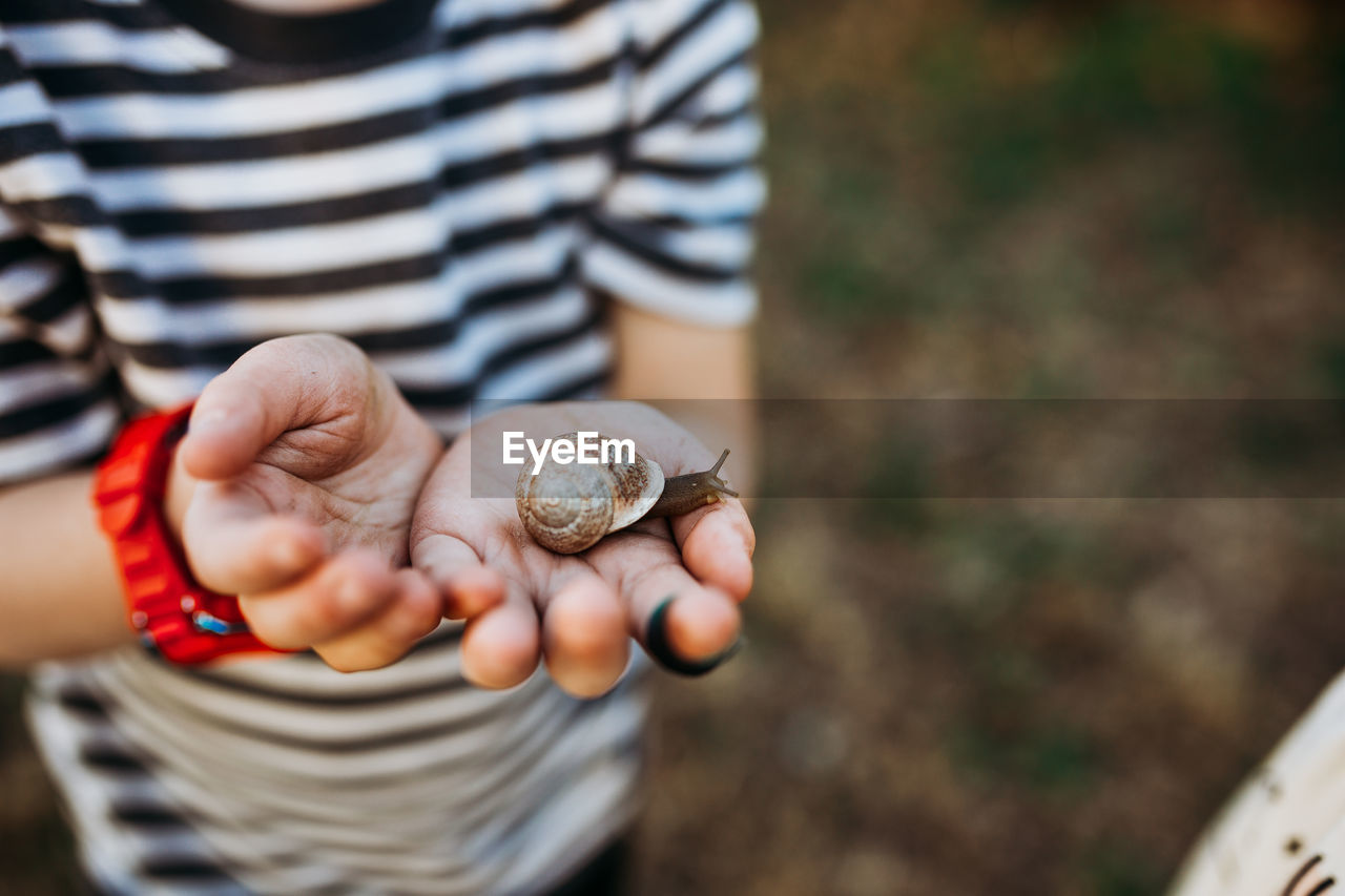 Close up of young boy outside holding snail in dirty hands